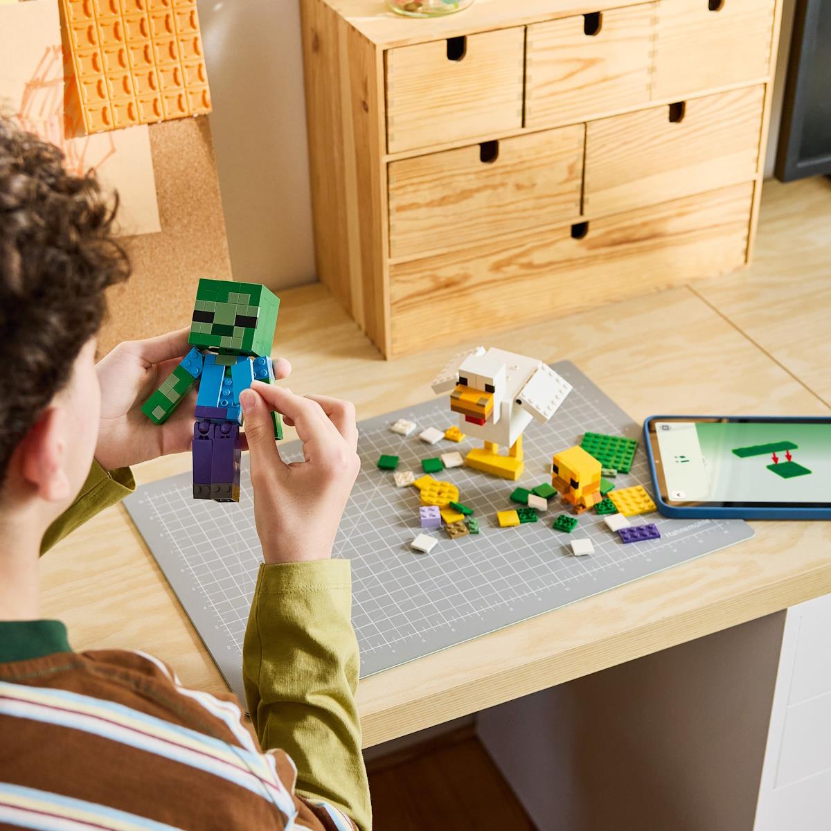 Pessoa segura brinquedo de blocos zumbi verde azul sobre mesa com peças e smartphone