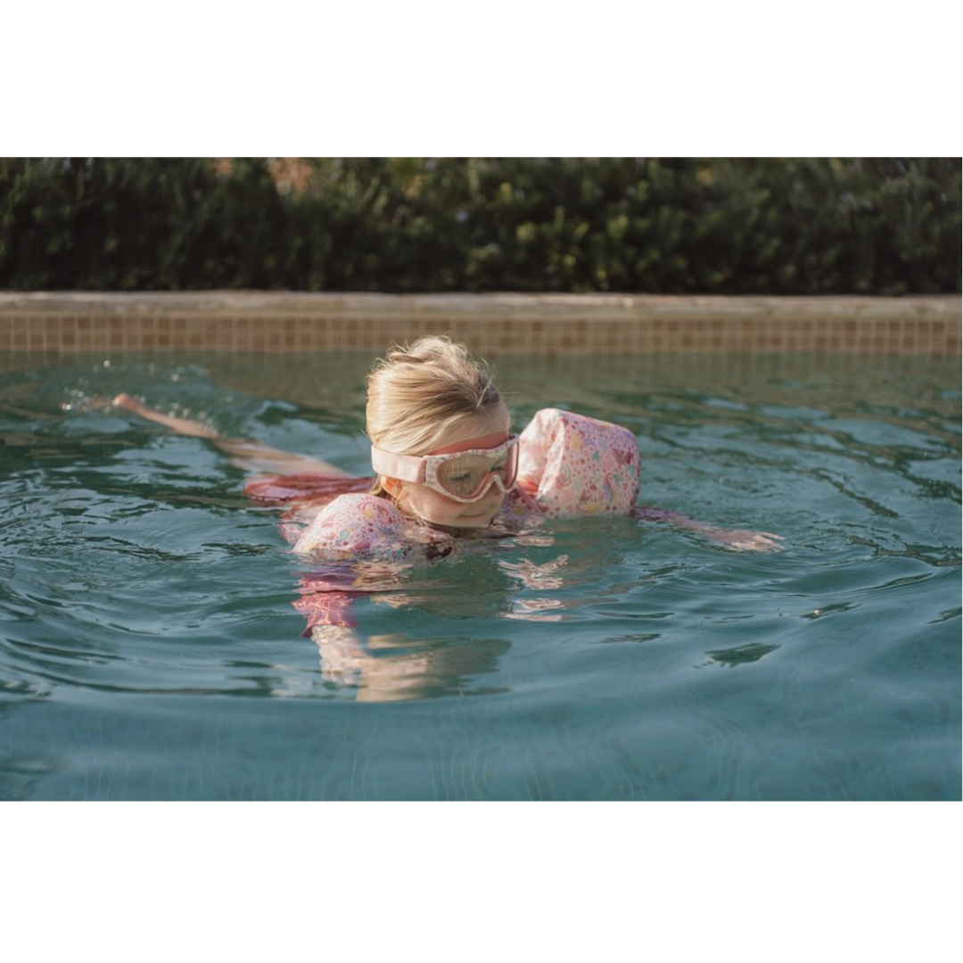 Criança a nadar numa piscina com óculos e bóias cor-de-rosa