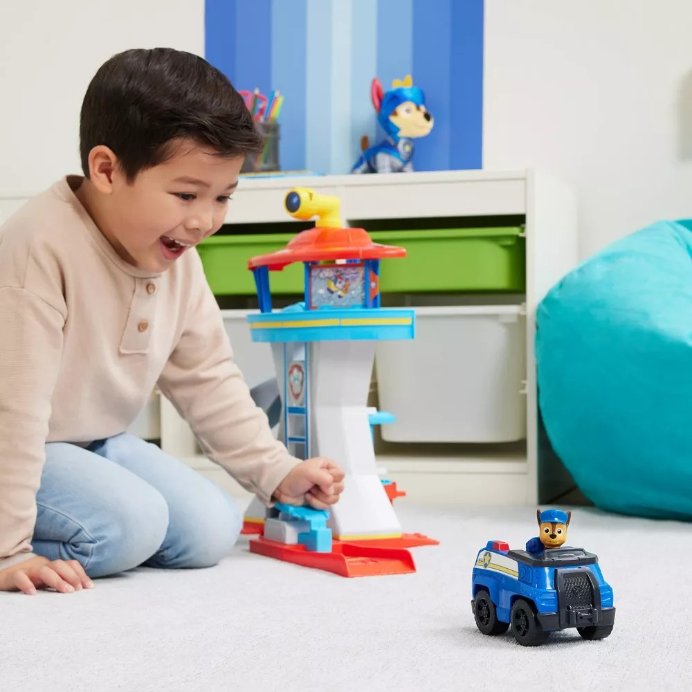 Criança brinca com brinquedo de torre e veículo azul em quarto com decoração azul e branca