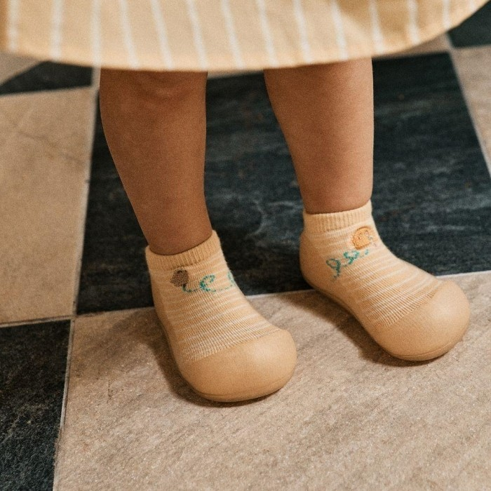 Sapatos meias bege com desenhos e texto azul e castanho em chão com azulejos variados.