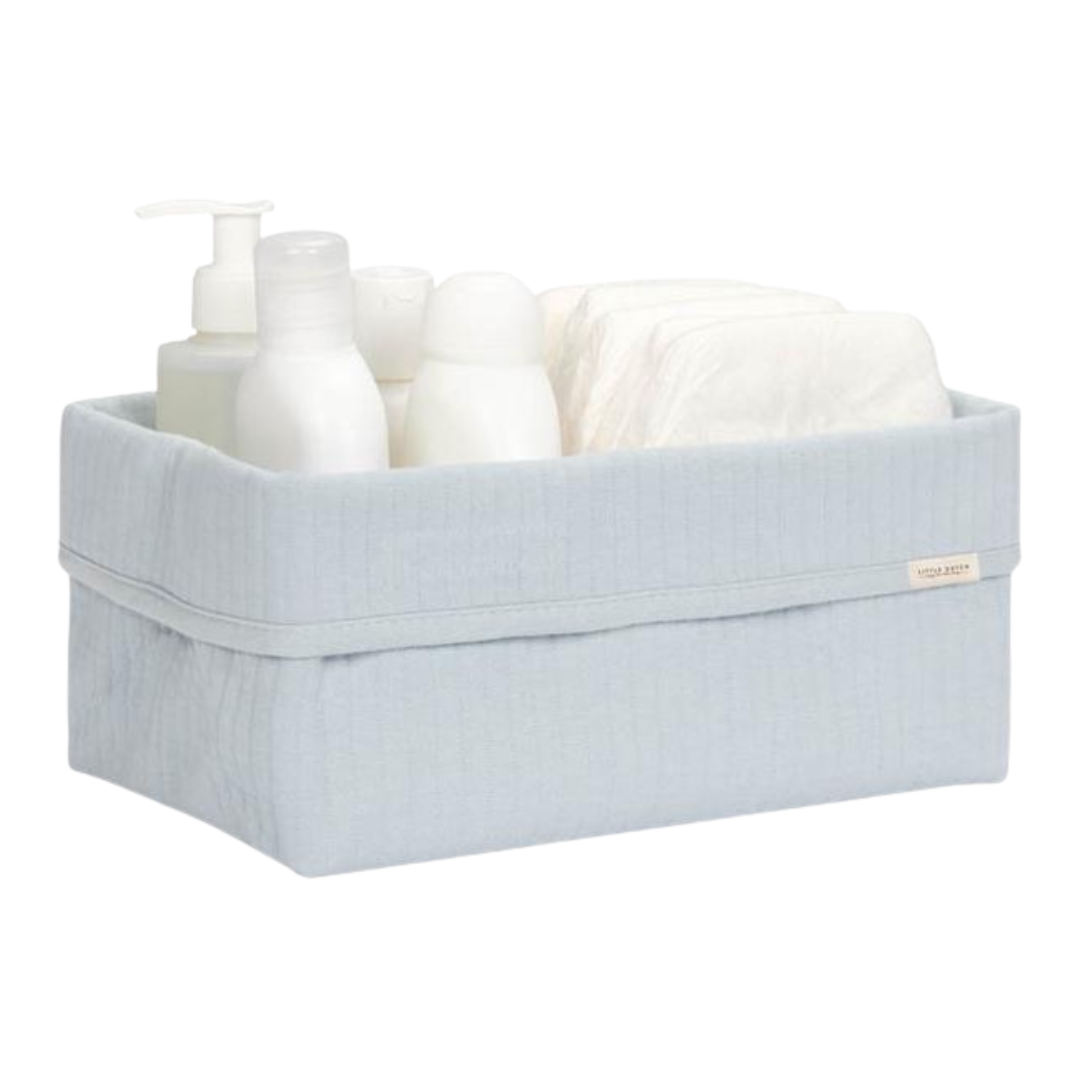 Cesto de tecido azul claro com produtos de higiene e toalhas.