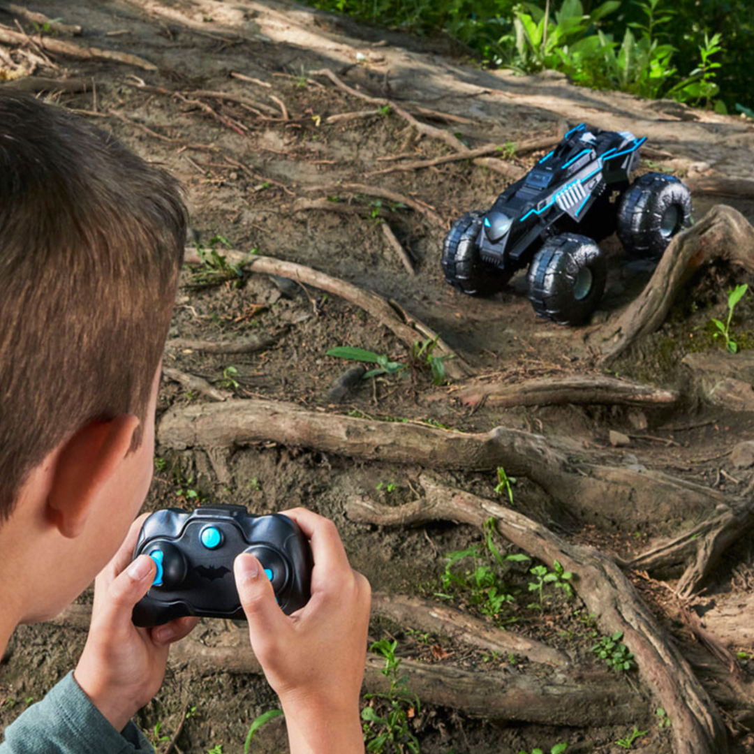 Criança controla carro de brinquedo todo-o-terreno preto com comandos.