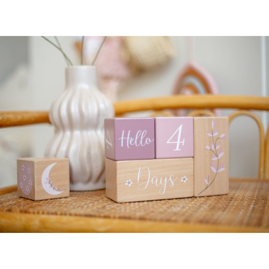 Blocos de madeira decorativos cor de rosa e natural com texto 'Hello 4 Days' ao lado de vaso branco