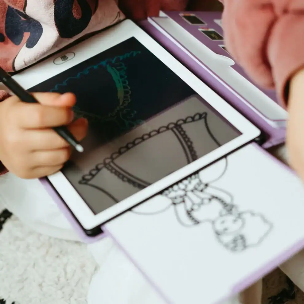 Tablet branco com capa lilás e caneta digital, com desenho de boneca no ecrã