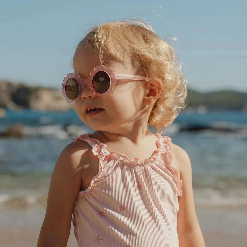 Criança de óculos de sol rosa e vestido rosa na praia