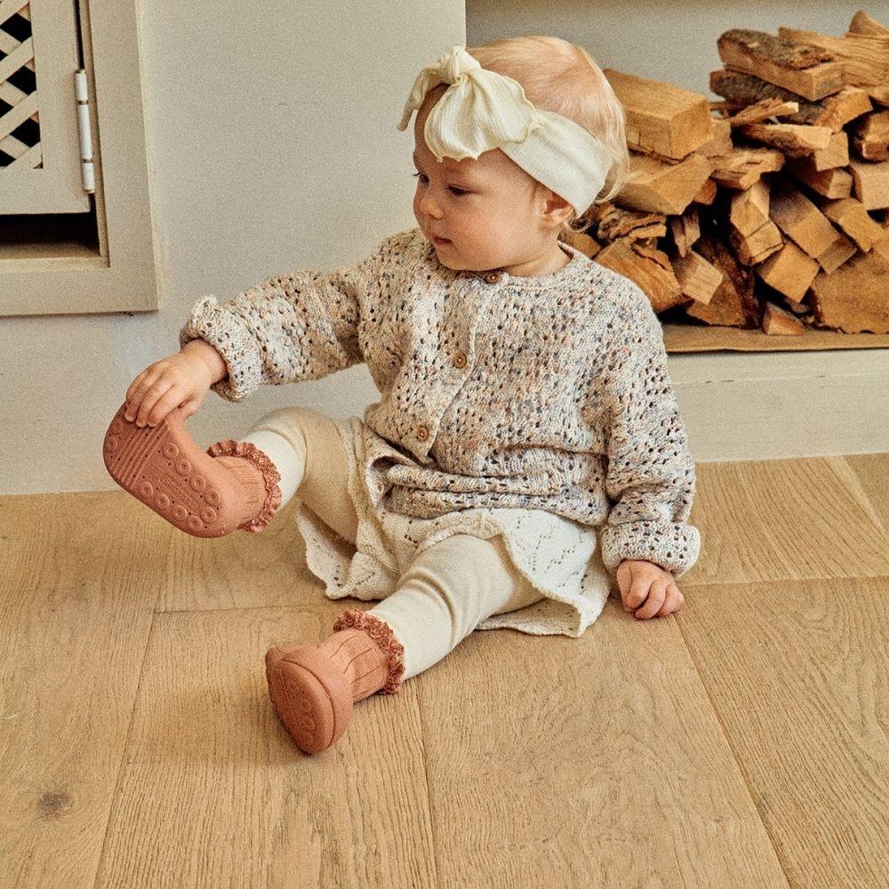 Bebé vestido com casaco de malha, leggings e faixa creme na cabeça sentado no chão de madeira