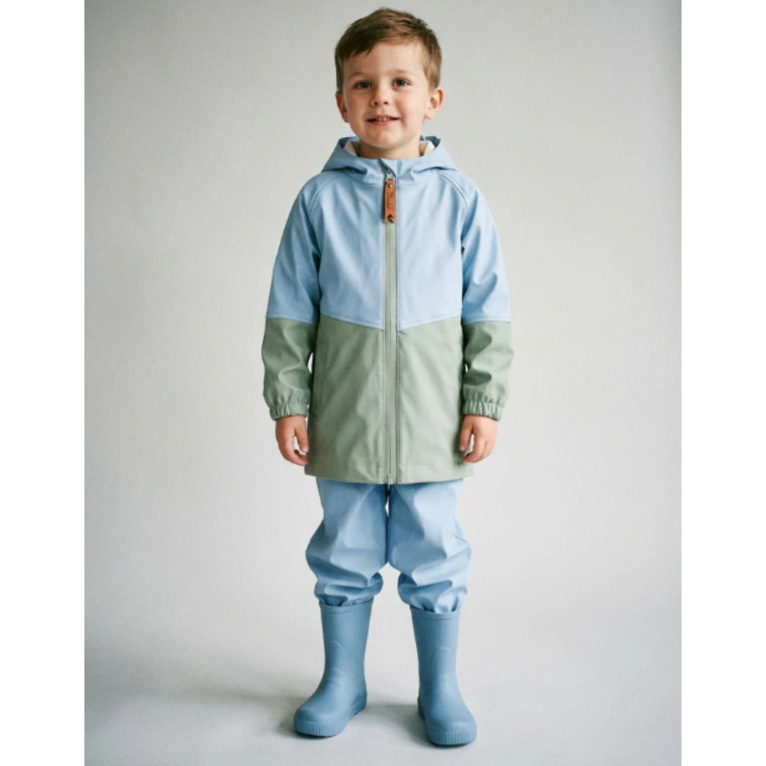 Menino de casaco e botas de chuva azuis e verdes em fundo branco.