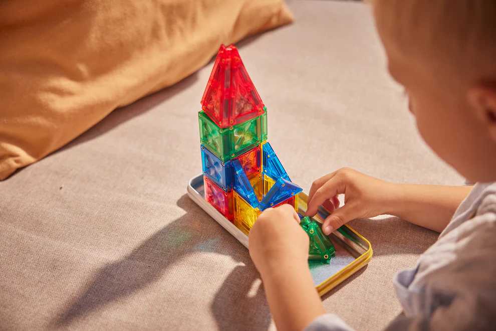 Brinquedo de construção magnético colorido montado por criança em tabuleiro metálico