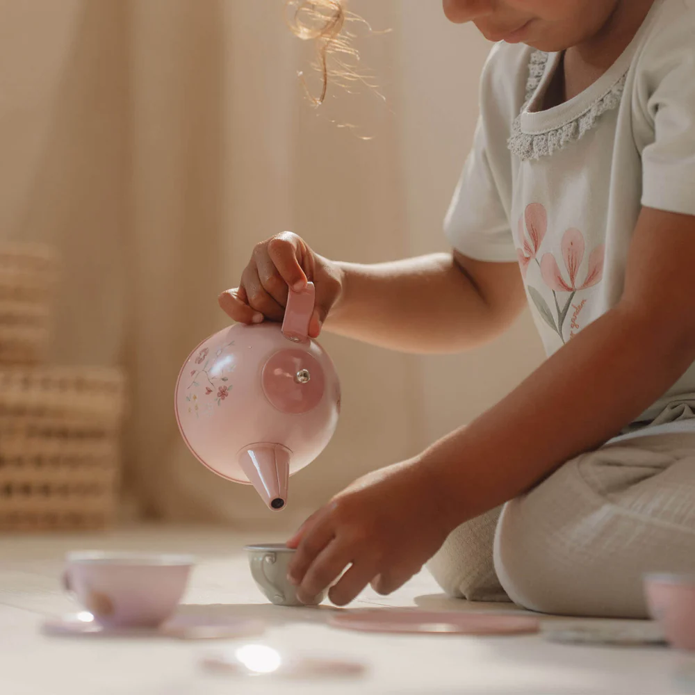 Criança a brincar com jogo de chá infantil rosa e branco no chão