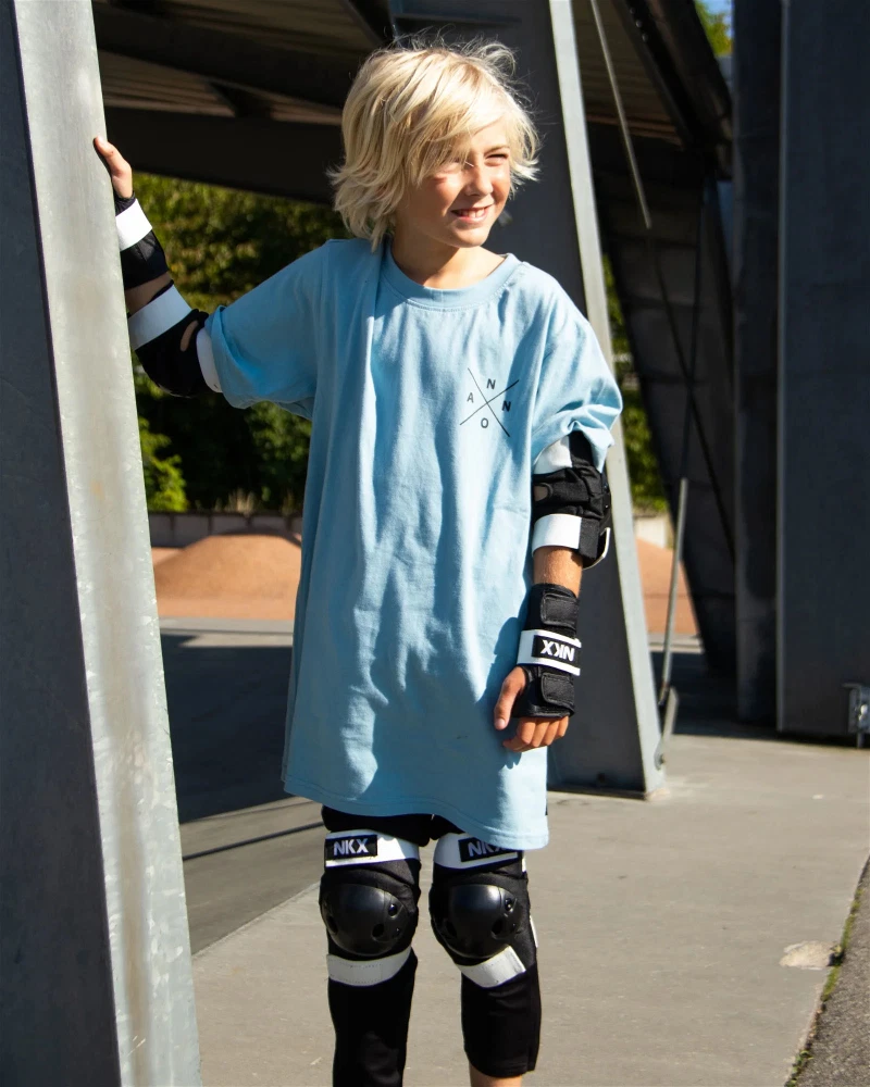 Camisola azul clara e equipamentos de proteção pretos para skate com detalhes em branco e texto NKX.
