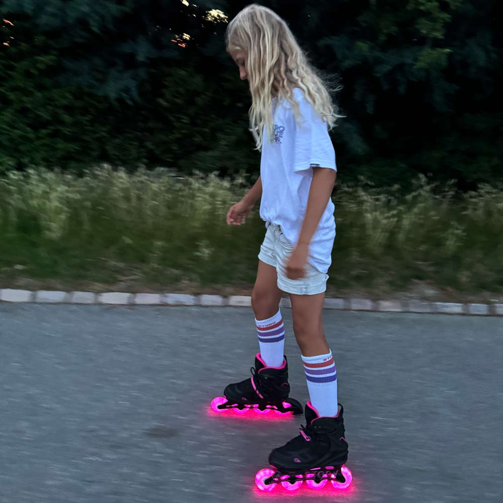Criança a usar patins em linha pretos com luzes LED cor de rosa e roupa casual numa área ao ar livre
