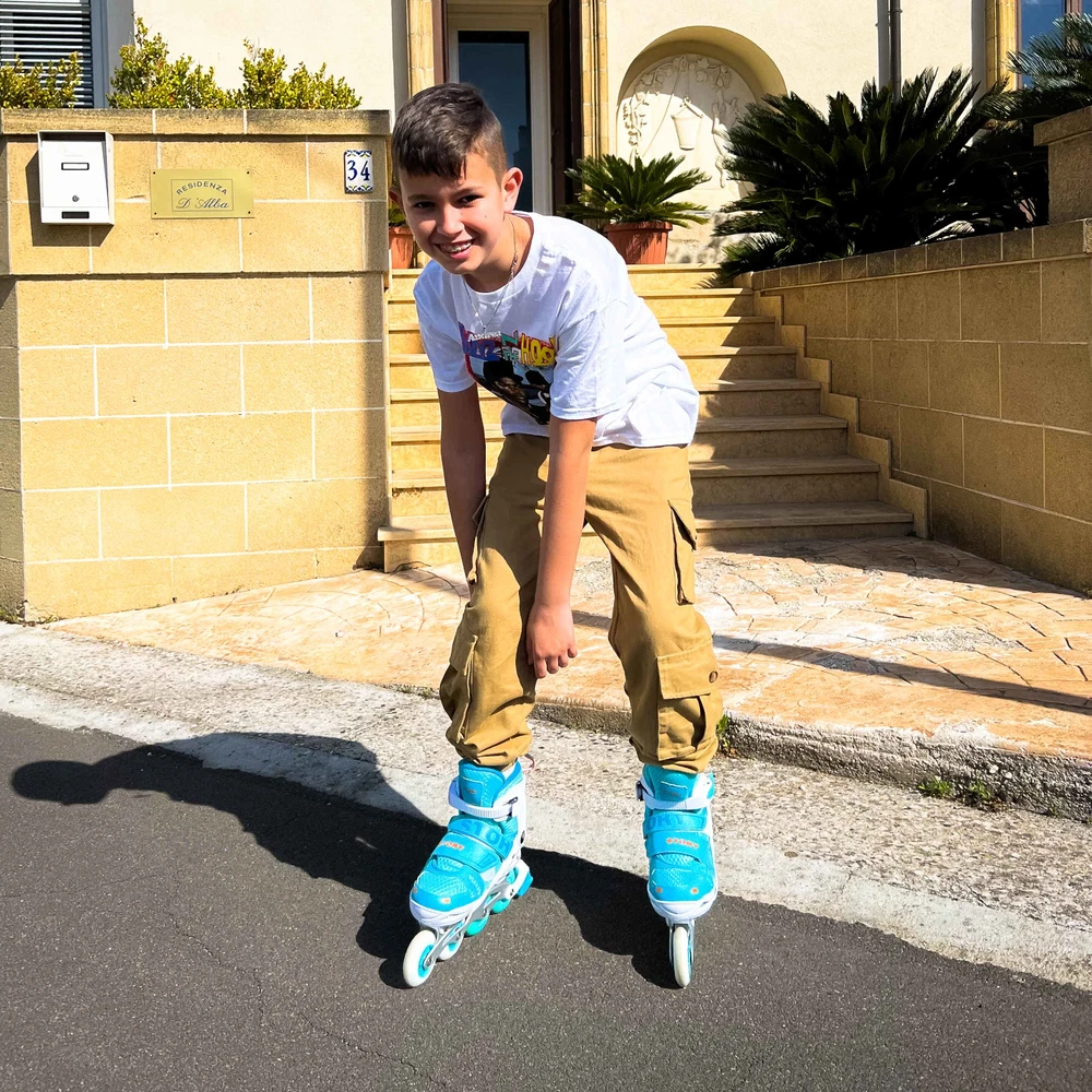 Rapaz com patins em linha azuis e brancos junto a uma escada e uma placa de moradia