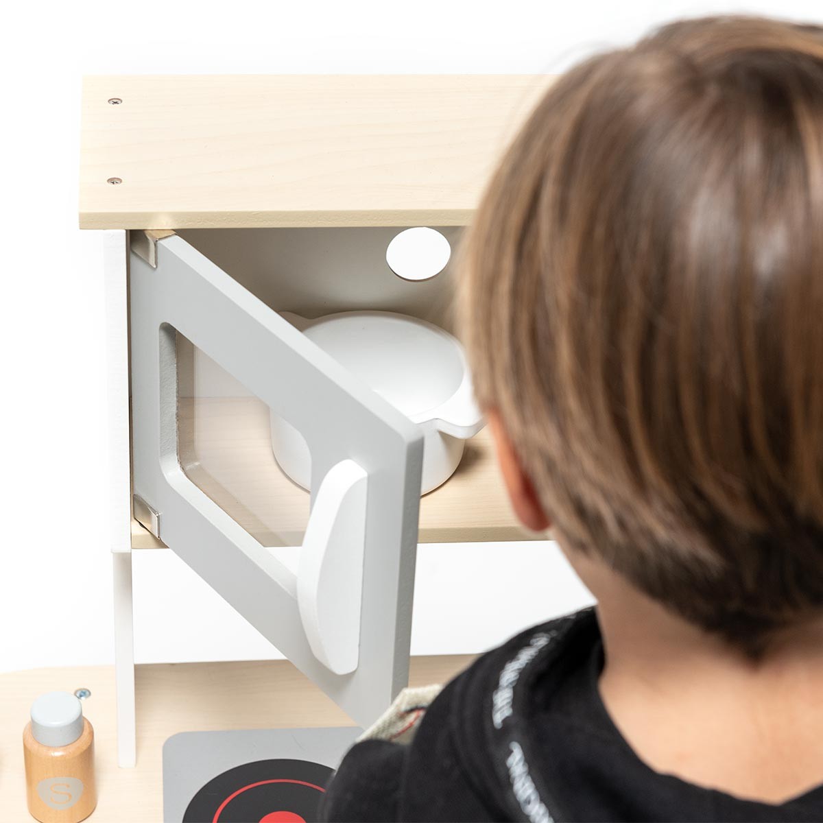 Cozinha de brinquedo com porta branca aberta e criança de costas