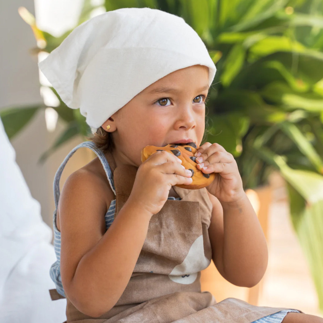 Criança com avental e lenço branco a comer biscoito decorado