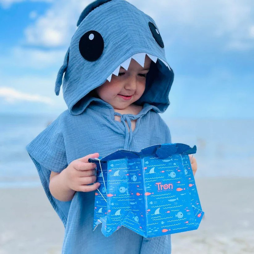 Criança de capa azul com capuz de tubarão e caixa azul decorada