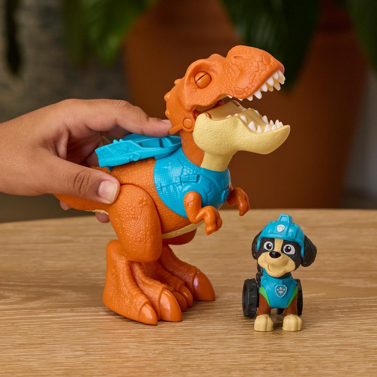 Brinquedo de dinossauro laranja e boneco de cão com capacete azul em mesa de madeira