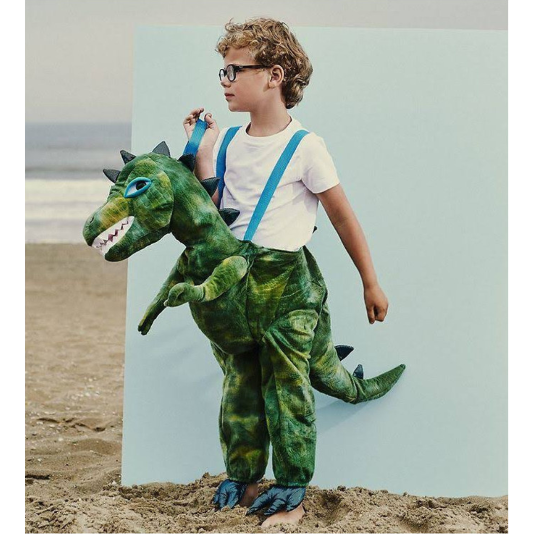 Menino com fato de dinossauro verde e suspensórios azuis na praia