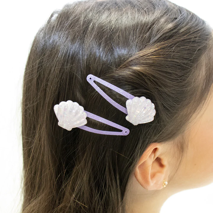 Duas molas de cabelo lilás com adornos brancos em forma de concha no cabelo castanho