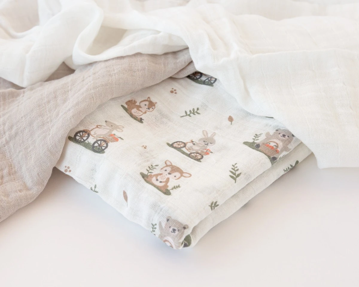 Três tecidos de algodão muselina para bebé, em branco, bege e com estampado de animais.