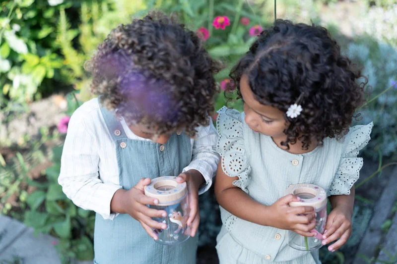 Crianças com potes transparentes e tampas de madeira em jardim