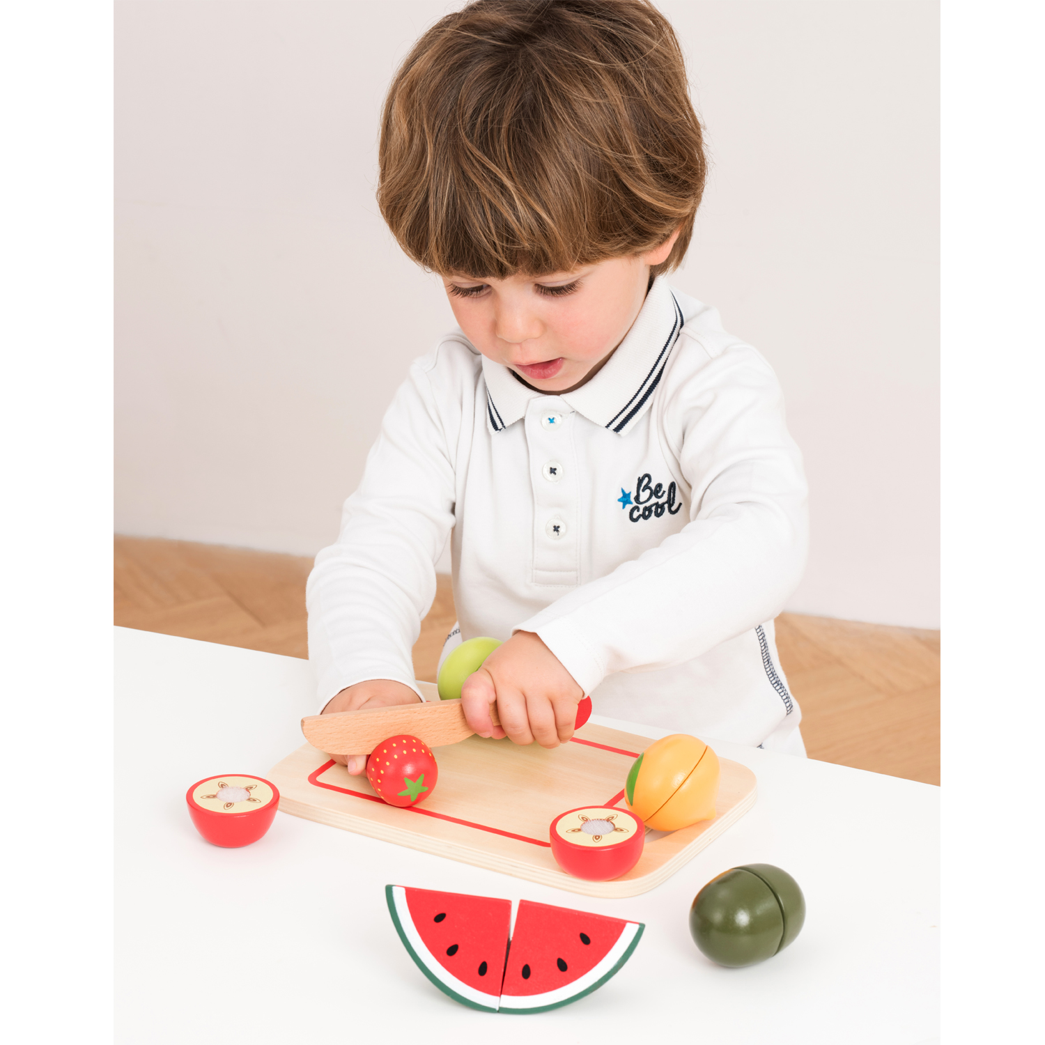 Criança com camisola branca a brincar com brinquedos de madeira em forma de frutas sobre mesa