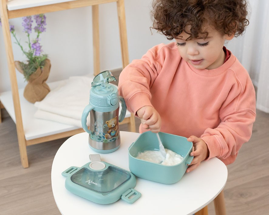 Garrafa de plástico azul e recipiente quadrado azul sobre mesa branca com criança mexendo o conteúdo