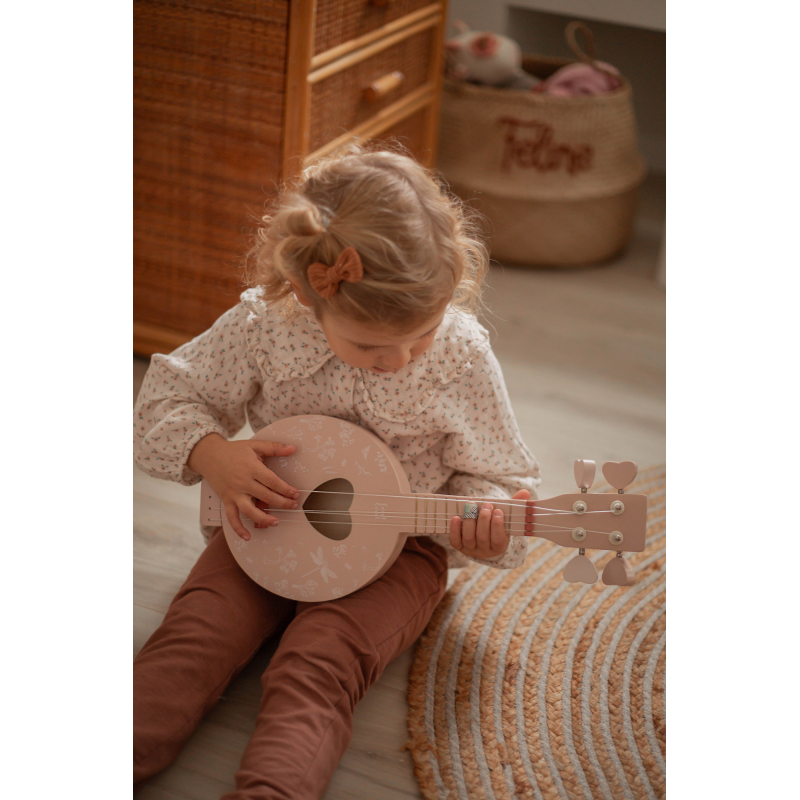 Criança a tocar ukulele rosa claro sentado no chão