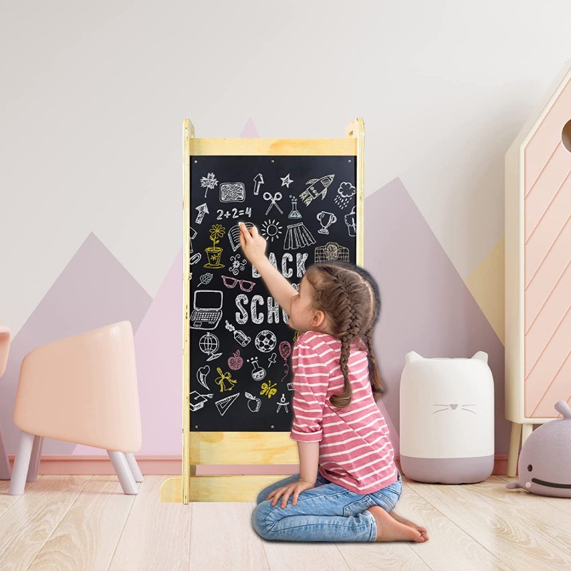 Menina a desenhar numa lousa preta numa sala infantil com móveis coloridos.