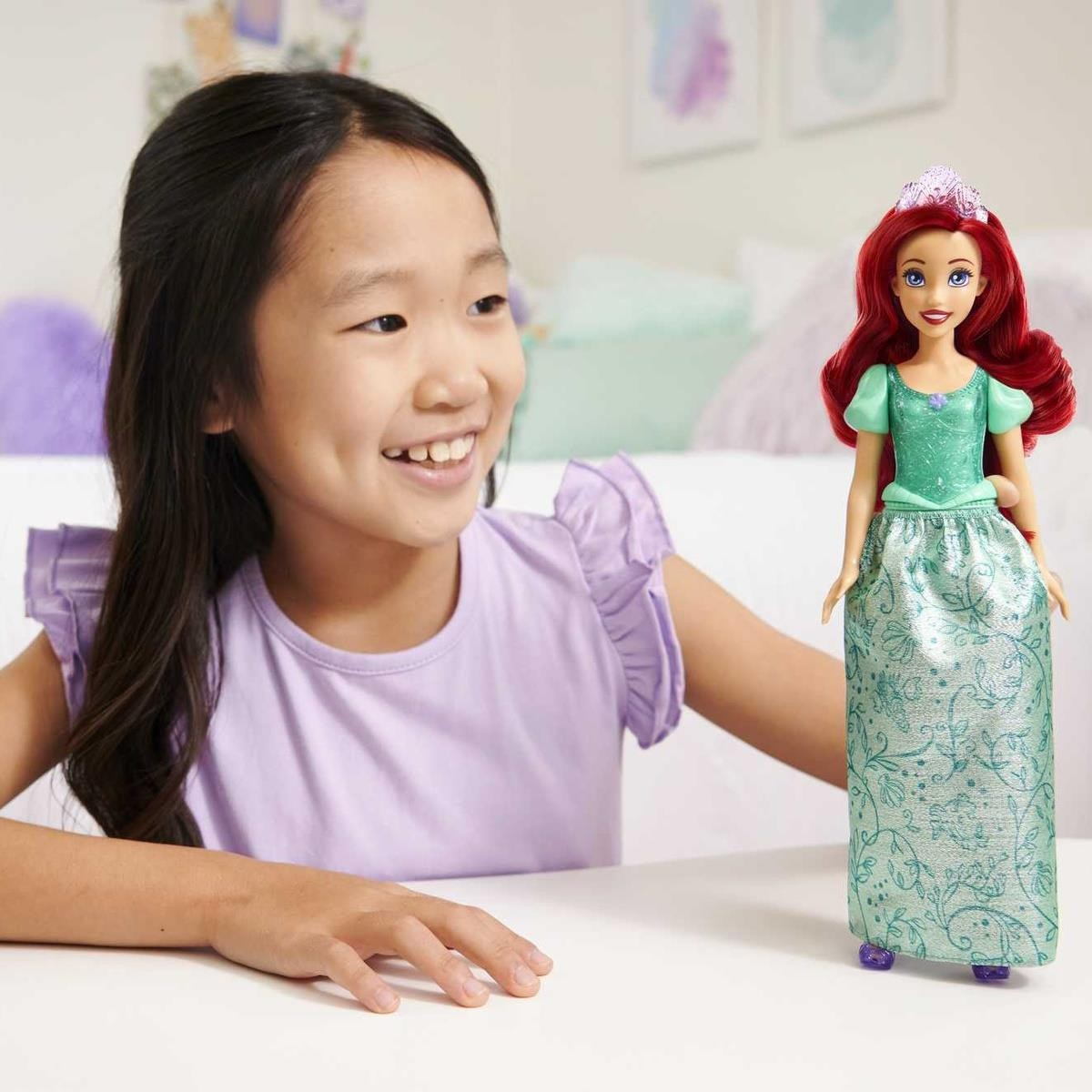 Boneca princesa verde com saia brilhante e tiara ao lado de criança sorridente em ambiente interior