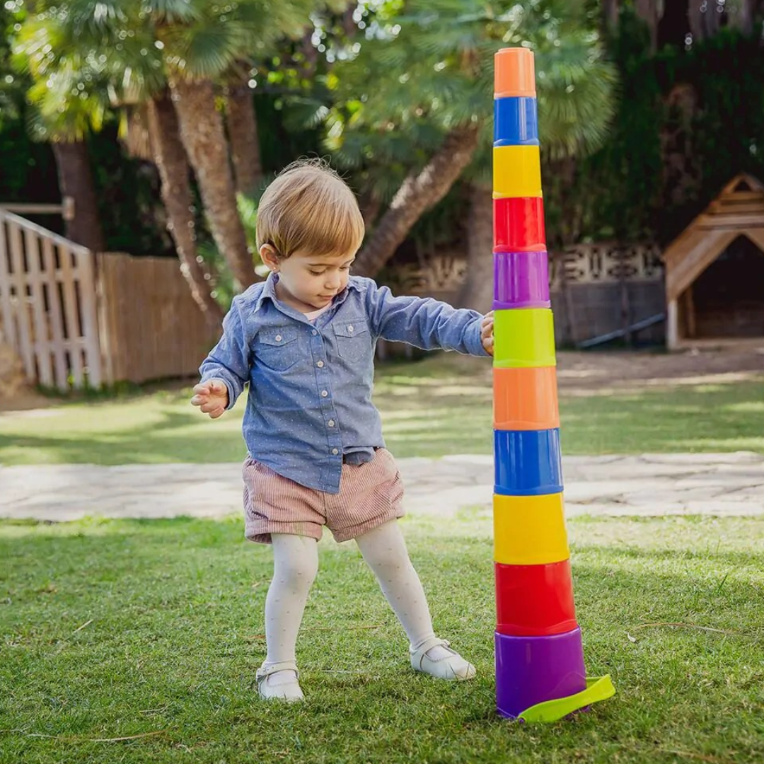 Criança a empilhar copos plásticos coloridos no jardim