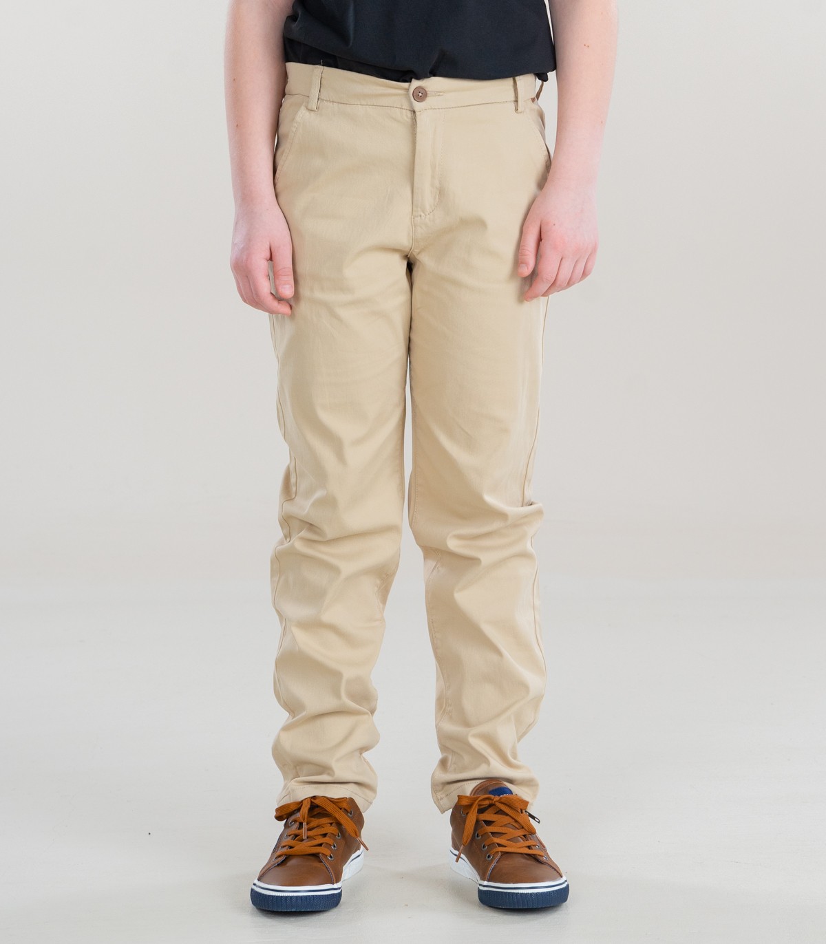 Calças bege de tecido liso e ténis castanhos em fundo cinza