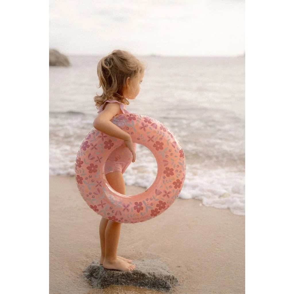 Criança de banho rosa com boia rosa florida na praia
