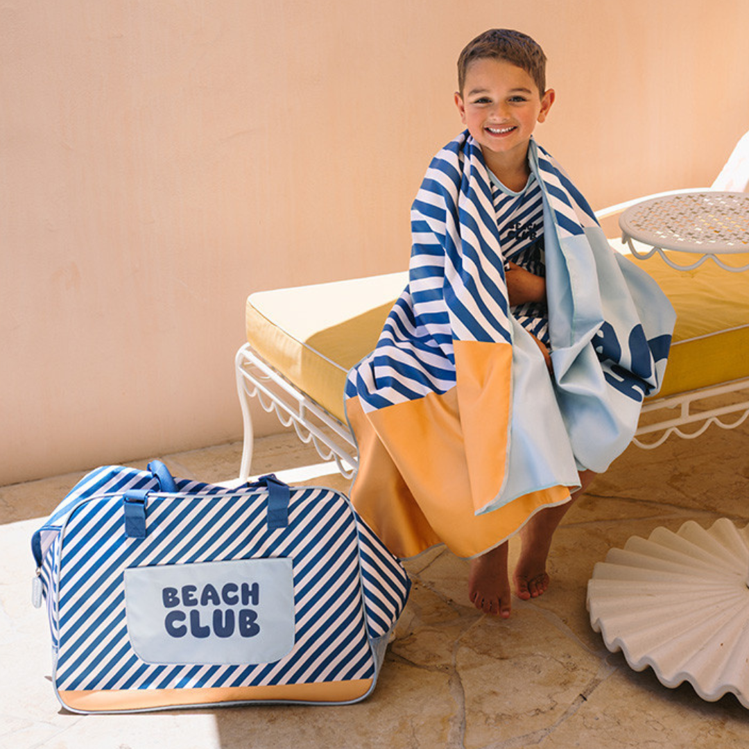 Criança com toalha às riscas e mala Beach Club