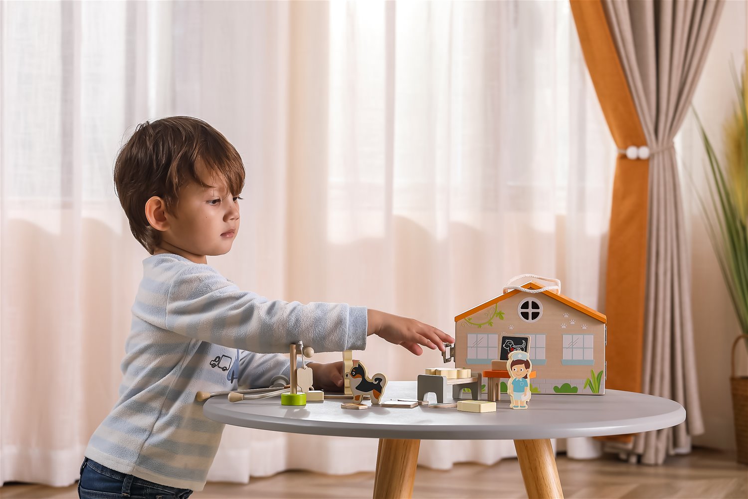 Criança a jogar com brinquedos de madeira de casa e personagens em mesa branca