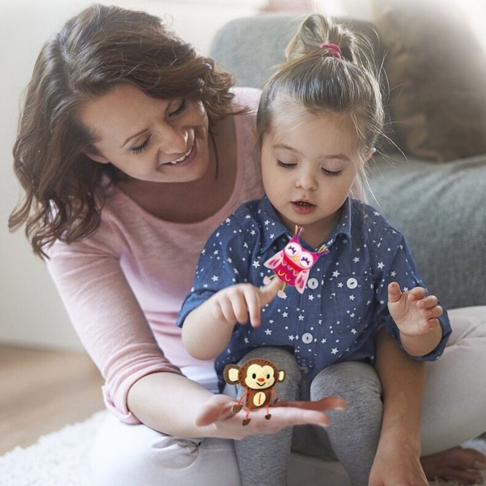 Criança com brinquedos de pelúcia coloridos sentada no colo de uma mulher sorridente com camisa rosa.