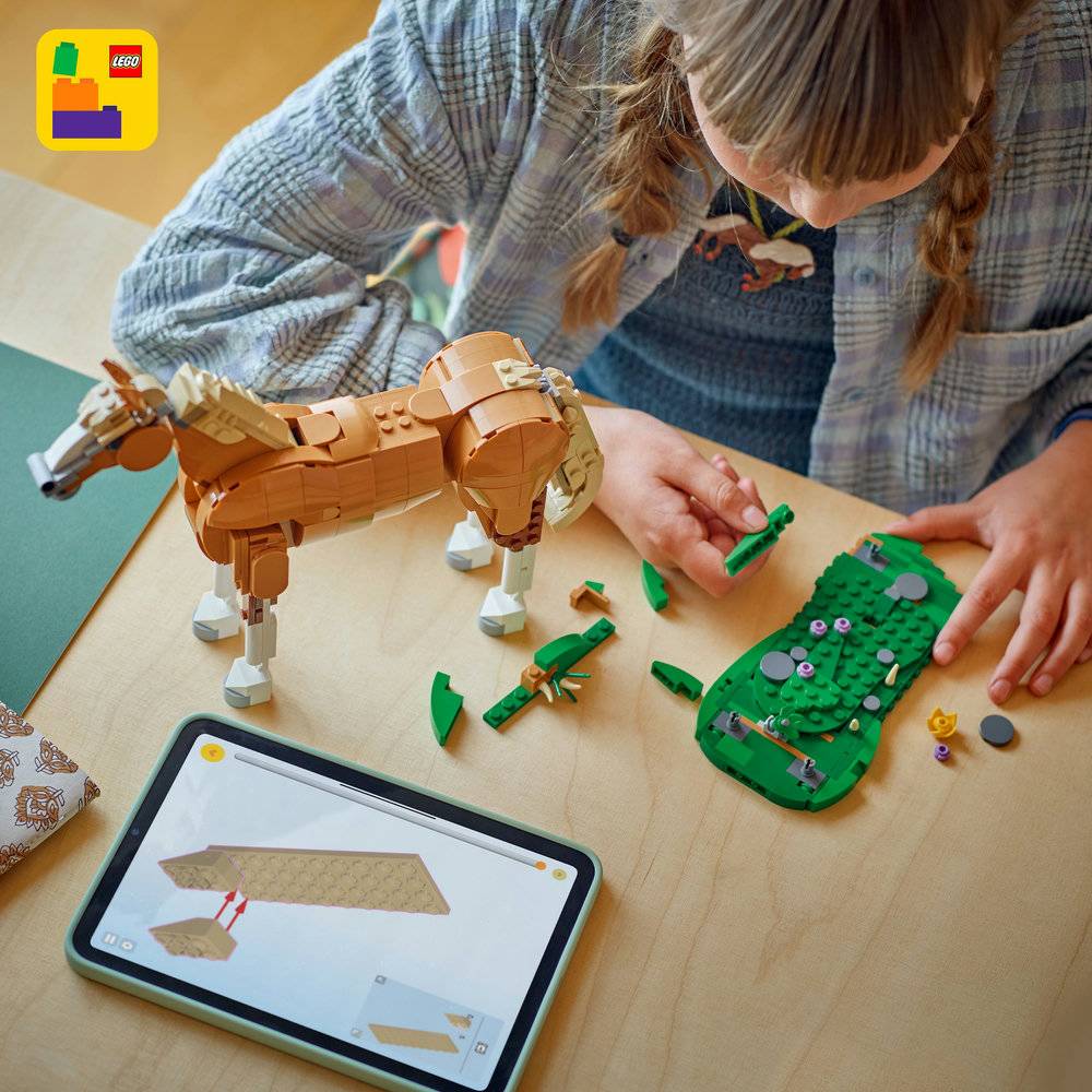 Pessoa a montar cavalo LEGO com peças de construção e tablet com instruções.