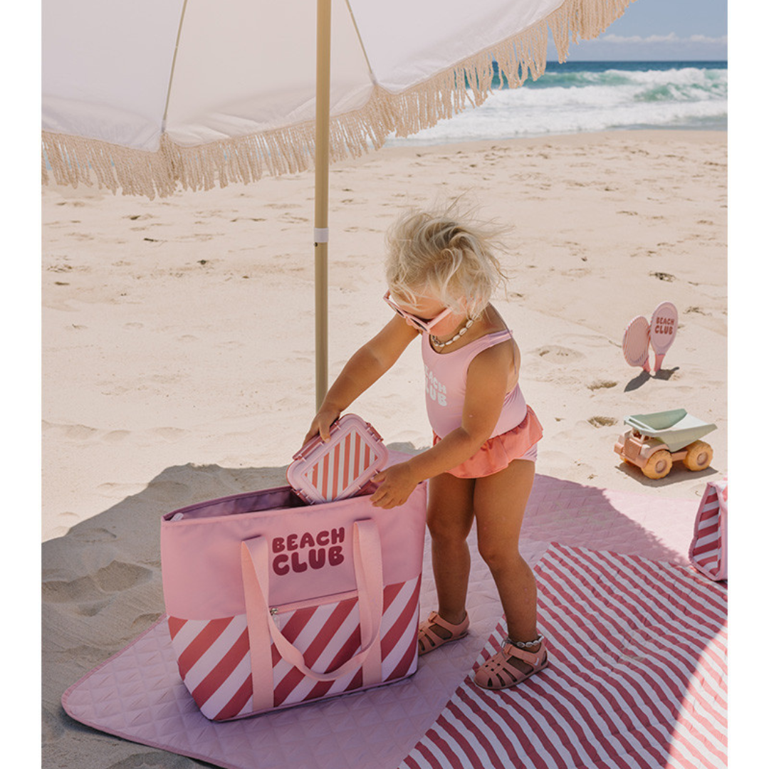 Menina pequena a brincar com bolsa e caixa rosa na praia