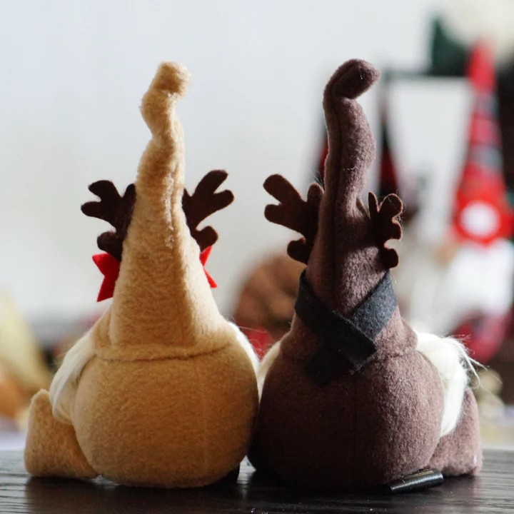 Brinquedos de pelúcia renas amarelo e castanho de costas sobre mesa de madeira