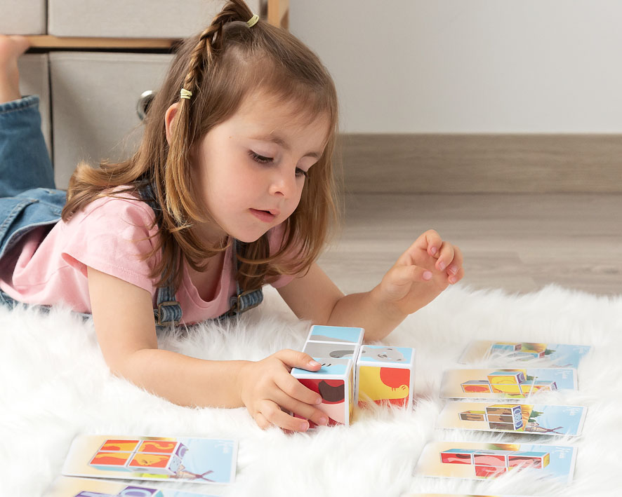 Criança a brincar com cubo mágico colorido e cartões de jogo num tapete branco
