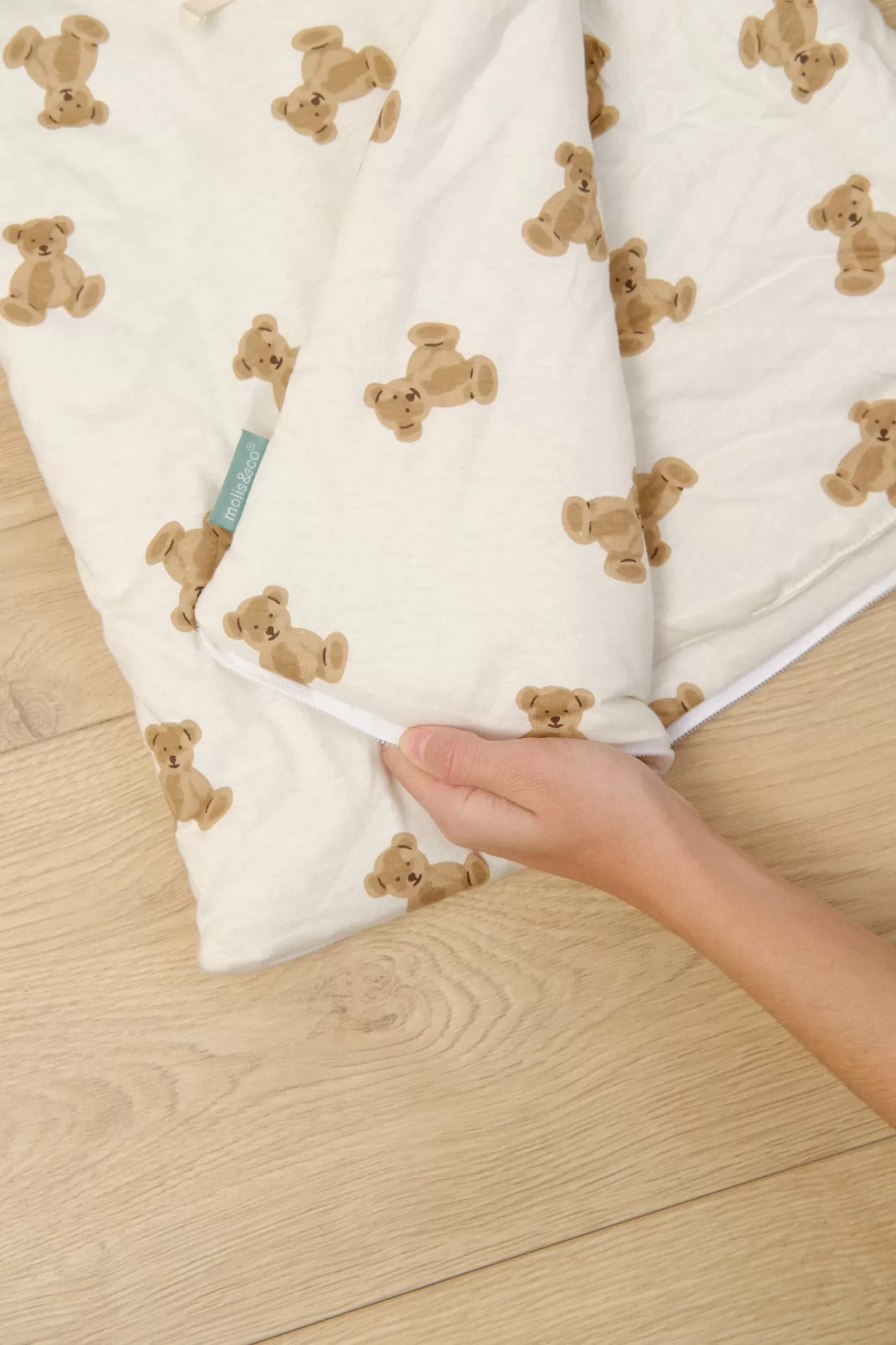 Tecido branco com padrão de ursinhos castanhos e fecho de correr, mão a segurar tecido.