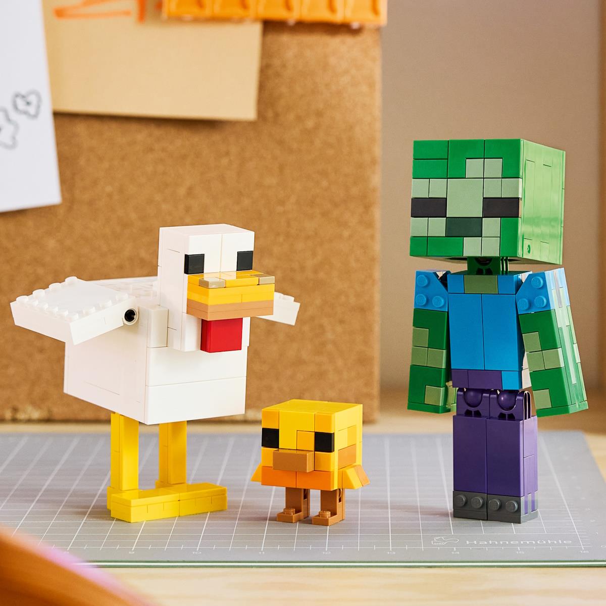 Figuras de blocos de construção tipo pixel de um pato, um patinho e um boneco verde com camisa azul sobre mesa.