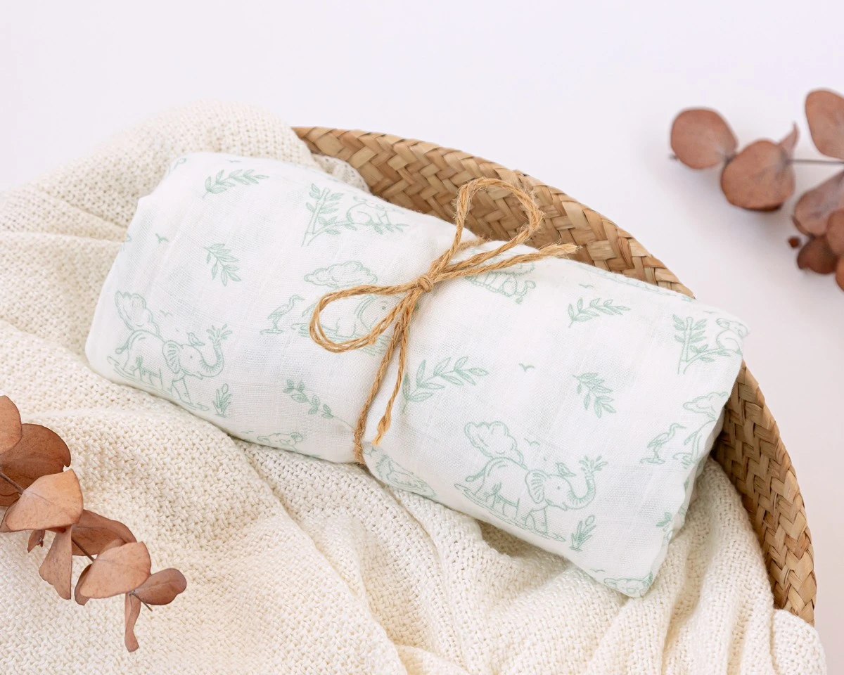 Pano com estampa de elefante e plantas amarrado com corda numa cesta de vime sobre tecido branco