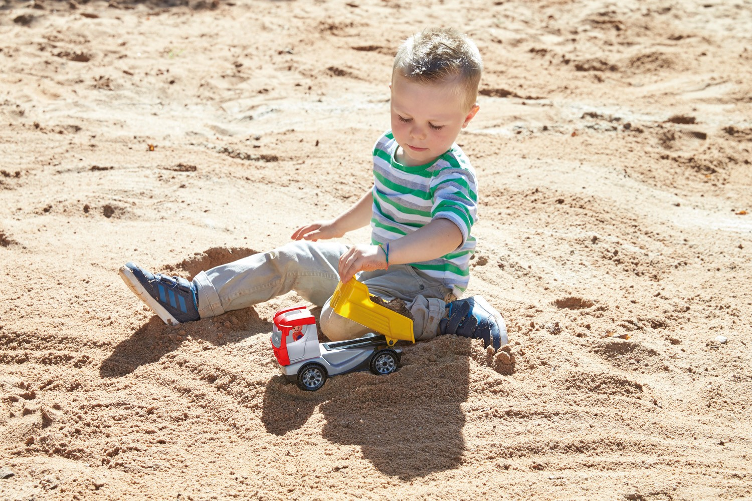 Criança a brincar com camião de brinquedo numa caixa de areia