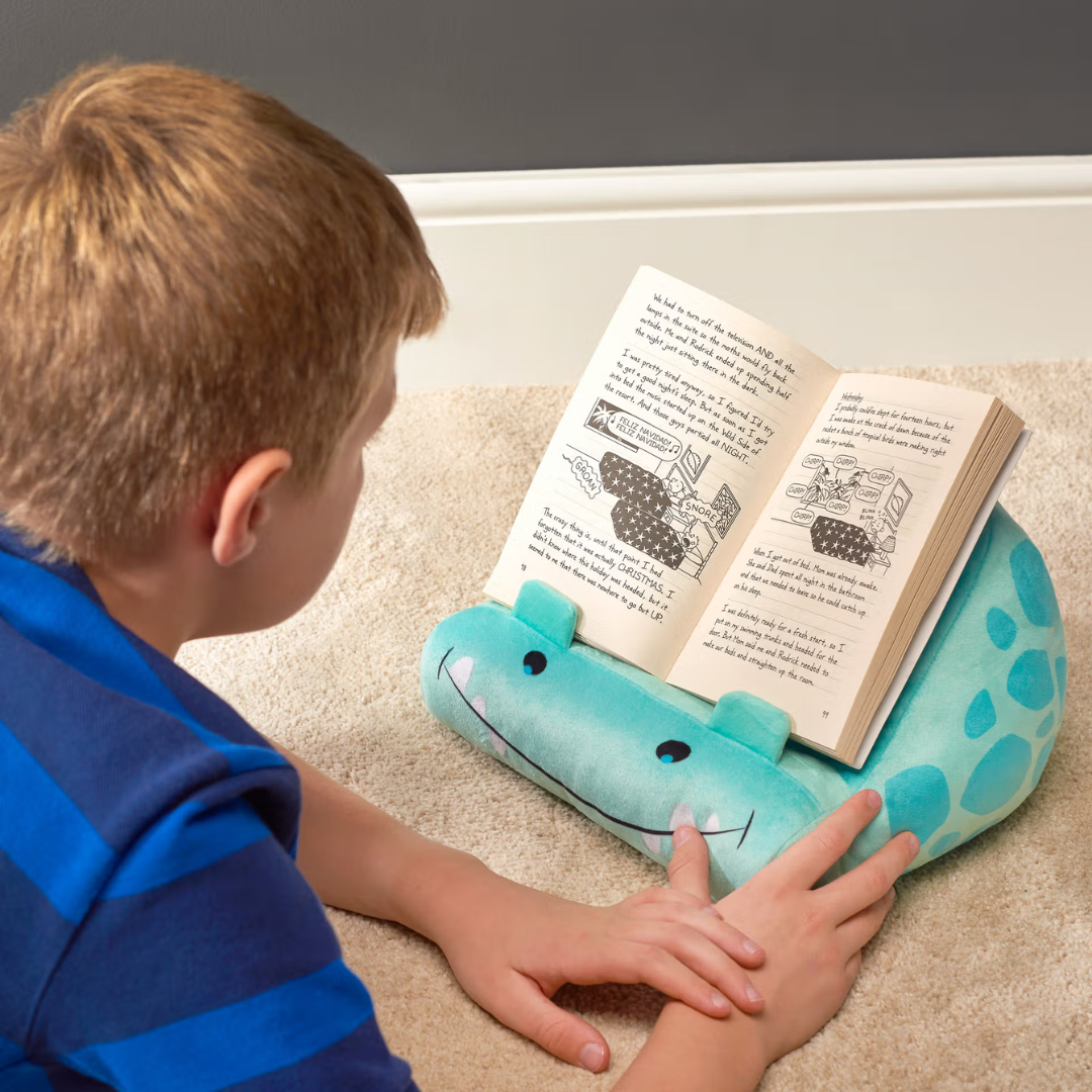 Criança lê livro apoiado em almofada de crocodilo azul