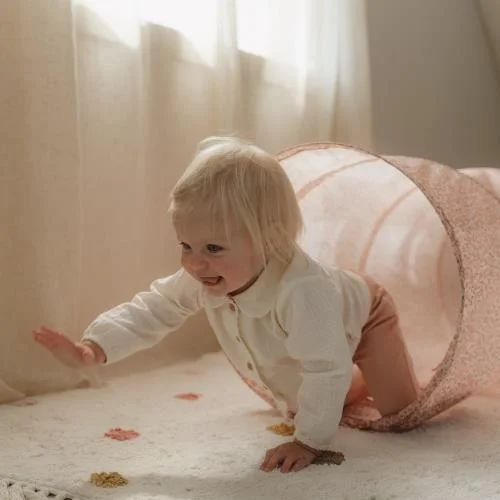 Bebé a sair de túnel de brincar rosa claro junto a cortinas brancas