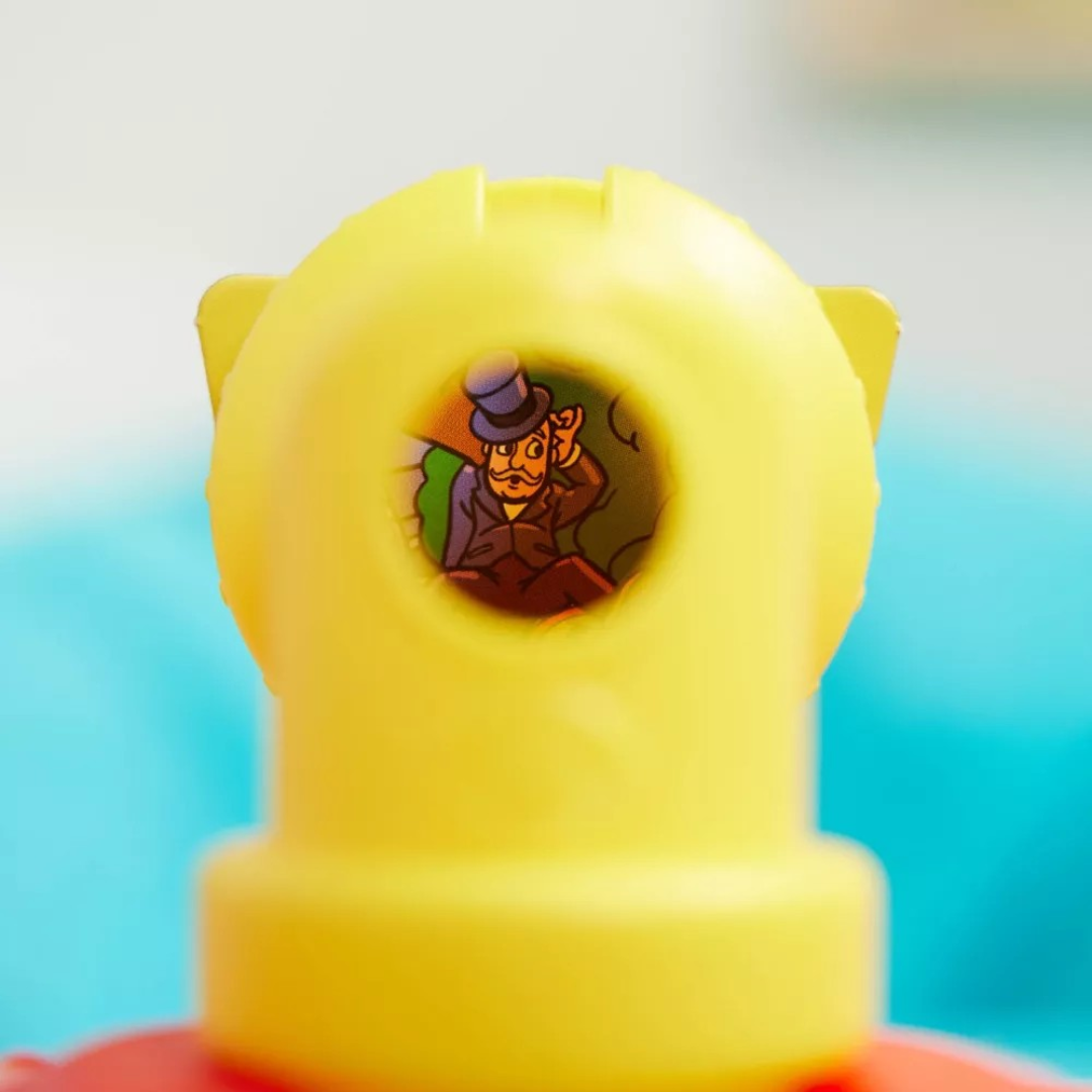 Brinquedo amarelo com figura de homem com chapéu visível através de orifício circular.