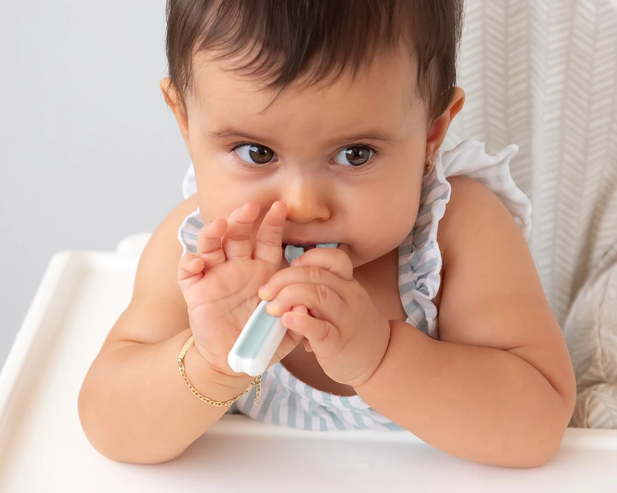 Bebé a morder um brinquedo ou mordedor azul claro e branco sentado numa cadeira alta