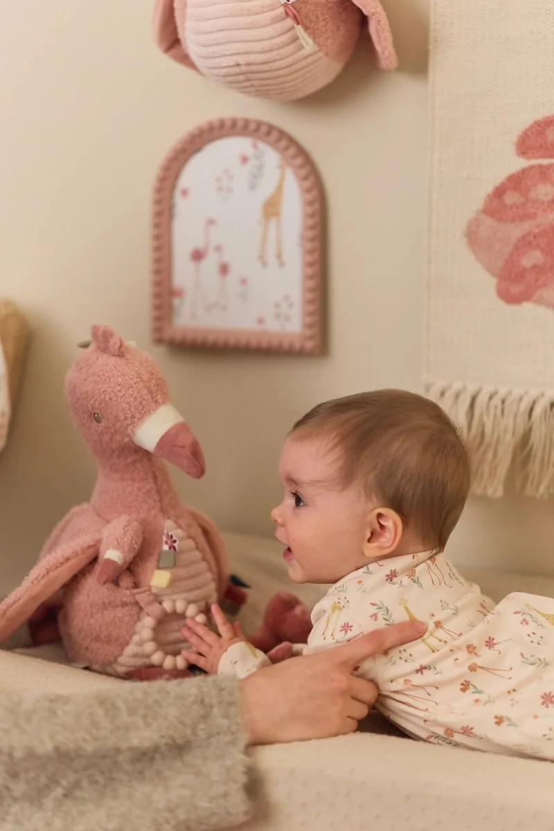 Bebé de macacão florido a tocar num peluche rosa de flamingo