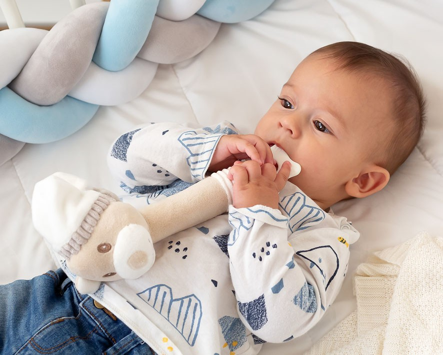 Bebé com brinquedo de pelúcia numa cama branca