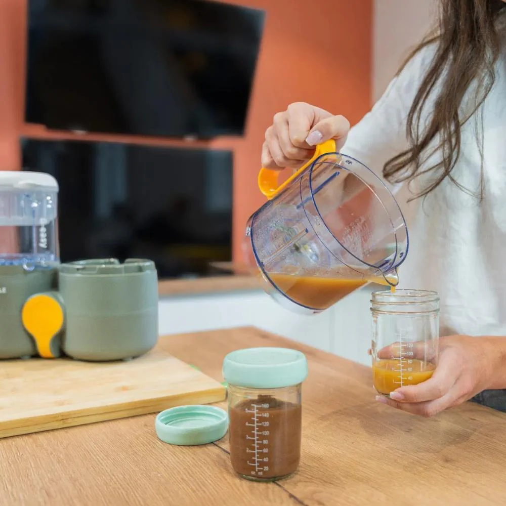 Frascos de vidro com tampa azul claro e jarro transparente a verter líquido castanho num ambiente de cozinha